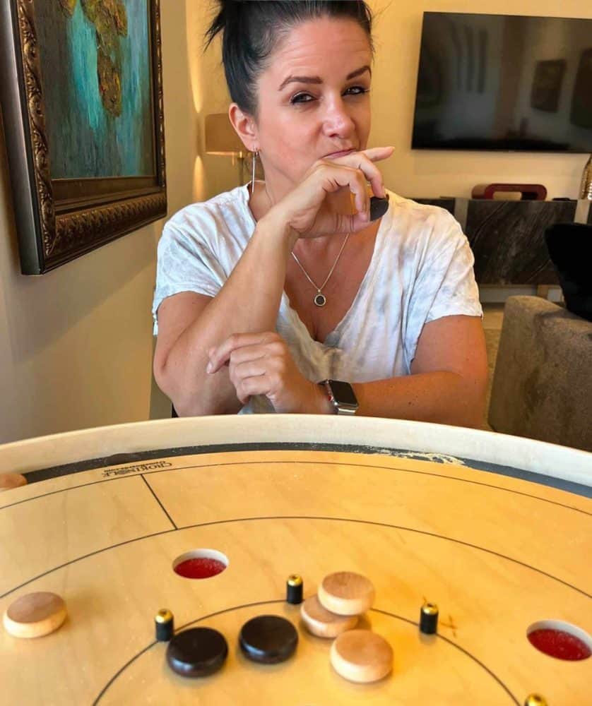 Crokinole player looks questioningly at the crokinole buttons stacked on top of one another while playing 5-hole crokinole
