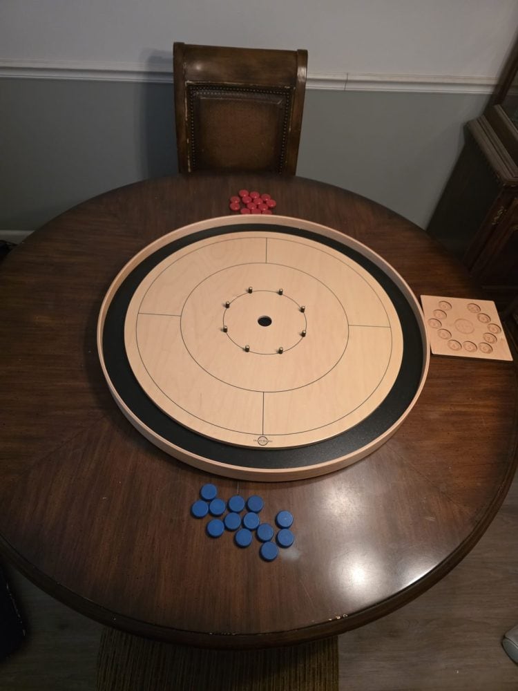 Cute cats sits beside Tracey crokinole board and swipes his paw at crokinole buttons