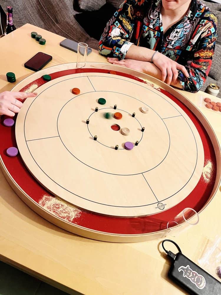 Cute cats sits beside Tracey crokinole board and swipes his paw at crokinole buttons